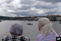 Two women watch a rescue vessel off the Margit bridge on the Danube river where a sightseeing boat had capsized in Budapest, Hungary, May 31, 2019.