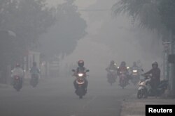 FILE - A resident drives a motorcycle through a haze produced by peatland fires at Suak Raya village in Aceh Barat, Aceh province, Indonesia, July 27, 2017 in this photo taken by Antara Foto.