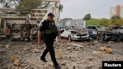 A police officer walks past the burnt cars of a humanitarian aid organization at the site of a Russian missile strike on an office building, amid the Russia-Ukraine conflict, in Kyiv, Ukraine, Sept. 2, 2024.