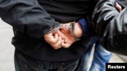 A man in handcuffs who was detained on suspicion of drug trafficking, is escorted by police outside the anti-drug unit of the National Police of Peru in Lima, August 16, 2013. REUTERS/Mariana Bazo (PERU - Tags: CRIME LAW DRUGS SOCIETY) - RTX12OBY