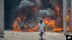 Seorang anak laki-laki berlari menjauh dari sebuah dealer mobil yang dibakar para pengunjuk rasa di Port-au-Prince, Haiti, 17 Maret 2021. 