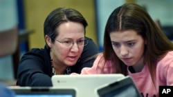 FILE - A teacher librarian at a Connecticut high school, left, works with a student in a Digital Student class, Dec. 20, 2017. The required class teaches media literacy skills and has the students scrutinize sources for their on-line information.