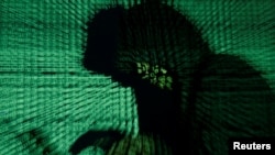 FILE - A man holds a laptop computer as cyber code is projected in this illustration taken May 13, 2017. A top U.S. cybersecurity official says various measures designed to cut Russia off from the West has led to a decline in ransomware attacks.