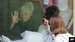 Judie Shape, left, who has tested positive for the coronavirus, waves to her daughter, Lori Spencer, right, as they visit on the phone and look at each other through a window at the Life Care Center in Kirkland, Wash., March 11, 2020.