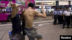 FILE - A pro-China demonstrator (L) hits a localist protester as police standing guard on the street look on during an anti-China protest at Mongkok shopping district in Hong Kong, June 28, 2015.