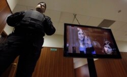 FILE - A bailiff stands next to a screen with a live broadcast of a court hearing on members of the female punk band 'Pussy Riot' in Moscow, Oct. 10, 2012.