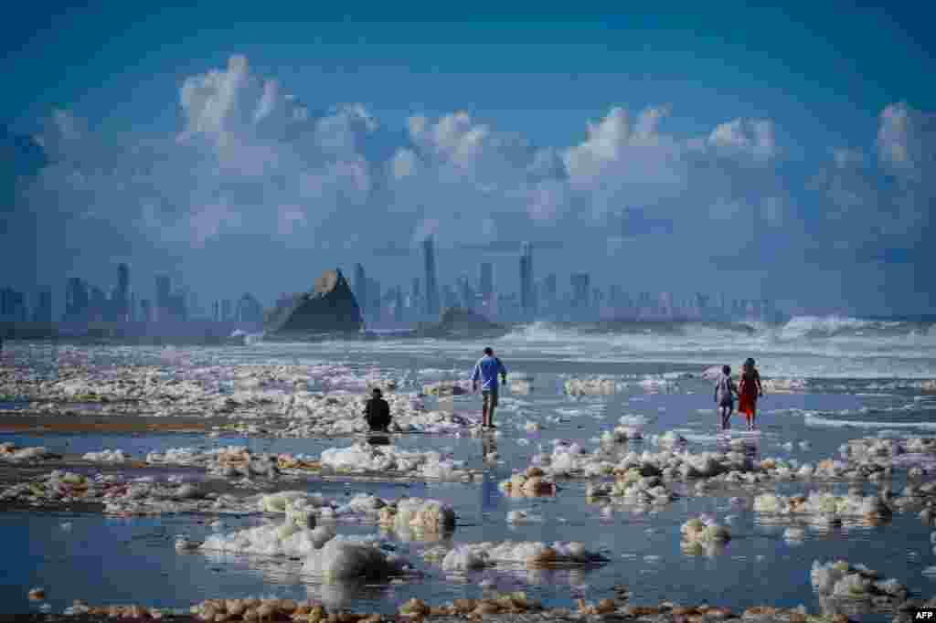 Tourists walk on the Currumbin Beach covered with foam in the wake of cyclonic conditions after wild weather lashed Australia&#39;s Northern New South Wales and South East Queensland with heavy rain, strong winds and king tides.