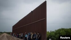 Solicitantes de asilo procedentes de Centroamérica esperan en el muro fronterizo entre México y EE.UU., en Penitas, Texas para entregarse a la patrulla. Abril 2 de 2019.