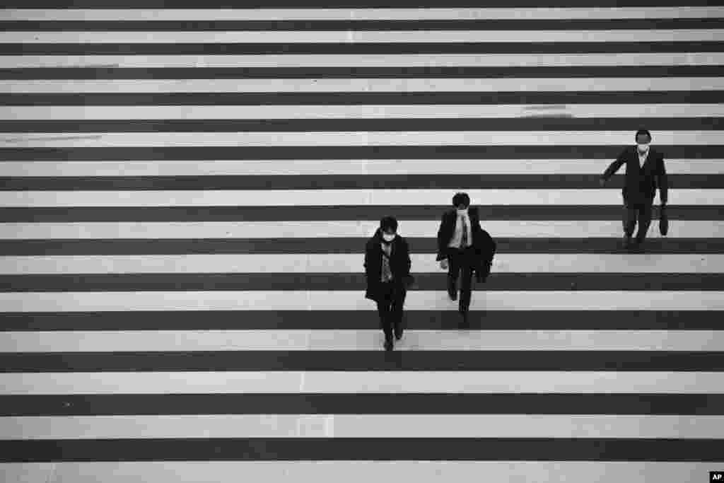 People wearing masks walk across a pedestrian crosswalk in Tokyo, Japan.