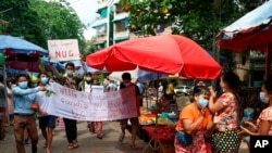 Anti-coup protesters hold signs that read 'We Support NUG,' which stands for ‘National Unity Government,’ as they march on a street where vendors sell fresh products April 17, 2021, in Yangon, Myanmar. 