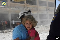 This photo provided by the Syrian Civil Defense, shows a White Helmets worker carrying a child after airstrikes hit a school housing a number of displaced people in the Daraa province of Syria, June 14, 2017.