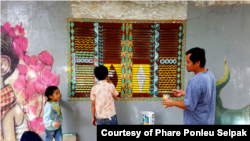 រូបឯកសារ៖ លោក​ ស្រី​ បណ្តូល ក្នុងពេលរៀបចំគូរគំនូរពណ៌លើផ្ទាំងជញ្ជែងអគារមួយ ក្នុងបរិវេណអង្គការហ្វារពន្លឺសិល្បៈ។ (រូបថតផ្តល់ឲ្យដោយហ្វារពន្លឺសិល្បៈ)