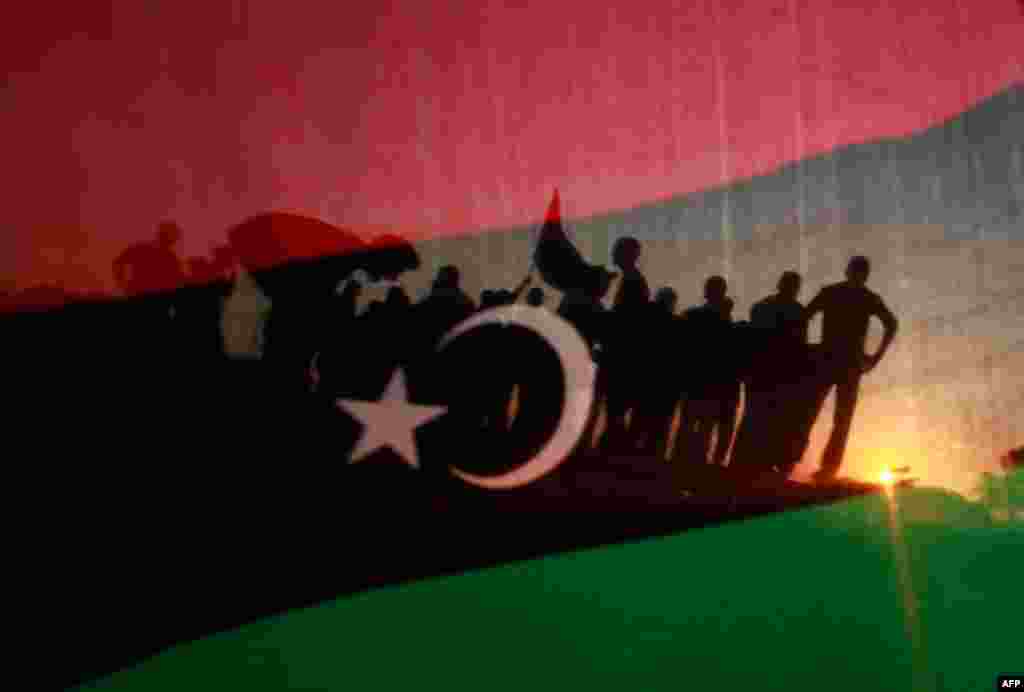 September 13: Libyans are seen through a Libya flag during a rally in front of the residence of Muammar Gaddafi in Tripoli. REUTERS/Suhaib Salem