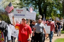 People hold signs as they walk past the governor's mansion to protest stay-at-home orders put into place due to the COVID-19 outbreak, April 21, 2020, in Jefferson City, Mo.