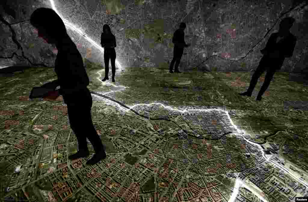 Museum staff walk with mobile devices over a giant illuminated aerial photograph of Berlin, including the marked course of the Berlin Wall and places related to the former East German Ministry for State Security (MfS), known as the Stasi, at the exhibition &#39;The Stasi in Berlin&#39; inside former Stasi prison, Hohenschoenhausen, Berlin.&nbsp;&nbsp;&nbsp;