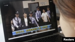 Seorang perempuan sedang mengamati berita yang menampilkan Gu Kailai dalam pengawalan ketat sedang memasuki ruang sidang pengadilan kota Hefei (9/8).
