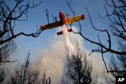 FILE - A firefighting plane drops its load during a forest fire near the village of Metohi north of Athens, Aug. 14, 2017.