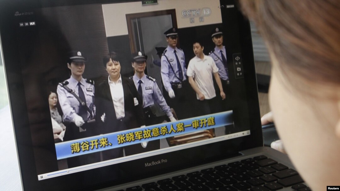 Seorang perempuan sedang mengamati berita yang menampilkan Gu Kailai dalam pengawalan ketat sedang memasuki ruang sidang pengadilan kota Hefei (9/8).