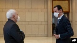 Sur cette photo publiée par l'agence de presse officielle syrienne SANA, le président syrien Bachar al-Assad, à droite, porte un masque alors qu'il s'entretient avec le ministre iranien des Affaires étrangères Mohammad Javad Zarif.