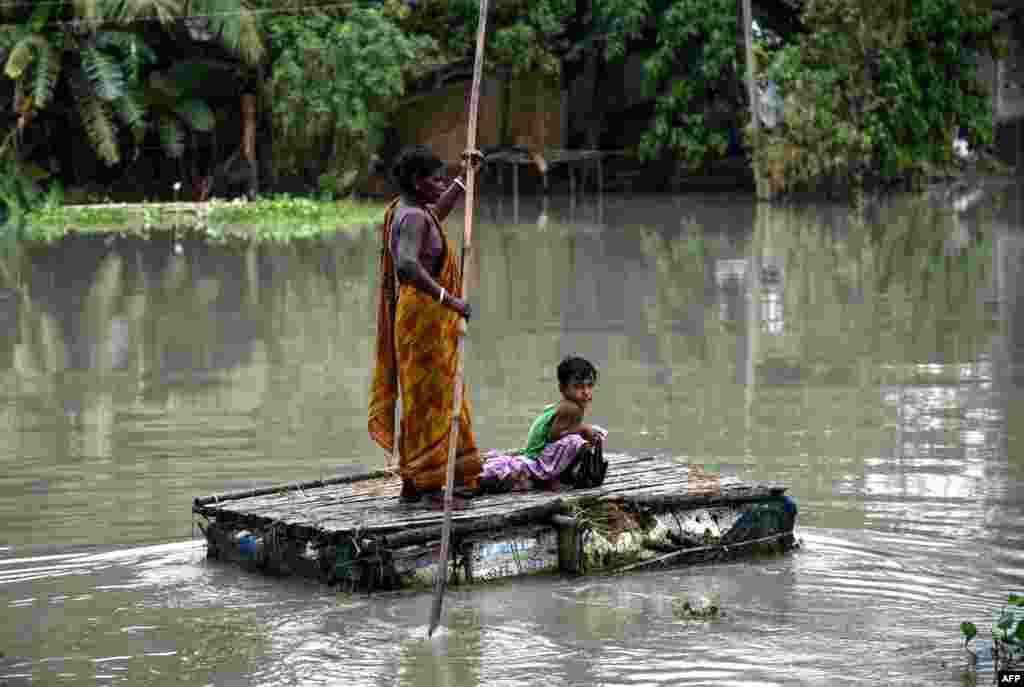 A woman paddles on a tinkered boat as a child looks on at the flood-affected Kayakuchi village in Barpeta district of the Assam state, India.