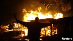 FILE - An opposition protester holds a machete in front of burning shops in Nairobi's Kibera slum, Dec. 30, 2007. Ten people have died in west Kenya as protests against Kibaki's controversial re-election erupted around the nation, the respected local…