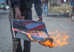 A Palestinian protester burns a poster with a picture of U.S. President Trump during minor clashes in the West Bank city of Ramallah, Jan. 30, 2020.