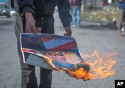 A Palestinian protester burns a poster with a picture of U.S. President Trump during minor clashes in the West Bank city of Ramallah, Jan. 30, 2020.