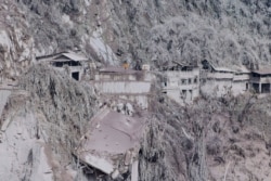 Abu menutupi rumah dan pepohonan di lereng Gunung Semeru di Lumajang pada 5 Desember 2021, sehari setelah letusan gunung berapi di gunung yang menewaskan sedikitnya 13 orang itu. (Foto: AFP/Aman Rochman)