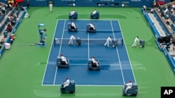 Una imagen repetida en las últimas cinco ediciones, los asistentes tratan de secar la cancha del estadio Arthur Ashe tras la lluvia.