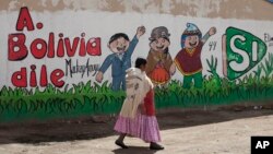 ແມ່ຍິງຊົນເຜົ່າ Aymara ຄົນໜຶ່ງກຳລັງຍ່າງຜ່ານຝາທີ່ມີຕົວ
ໜັງສືຂຽນເປັນພາສາ ສເປນ "Tell Bolivia Yes," ຫຼື "ບອກ ໂບລີເວຍວ່າ ແມ່ນ" ໃນການສະໜັບສະໜູນປະທານາທິ ບໍດີ ທ່ານ Evo Morales, ໃນເມືອງ El Alto, ປະເທດ ໂບລີເວຍ, 20 ກຸມພາ, 2016. 