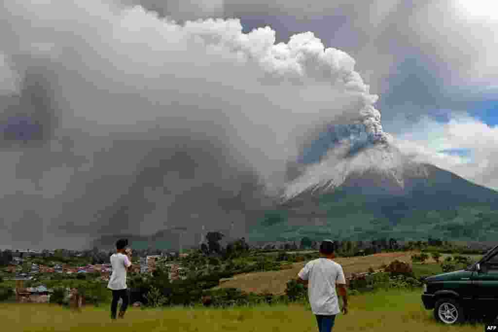 People look at Mount Sinabung spewing a massive column of smoke and ash as seen from Karo, North Sumatra, Indonesia.