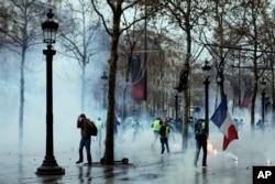 Demonstrators run away through tear gas during scuffles on the Champs-Elysees, Dec. 15, 2018, in Paris. Protests throughout the day against France's high cost of living by "yellow vest" demonstrators were largely peaceful.