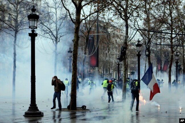 Demonstrators run away through tear gas during scuffles on the Champs-Elysees, Dec. 15, 2018, in Paris. Protests throughout the day against France's high cost of living by "yellow vest" demonstrators were largely peaceful.
