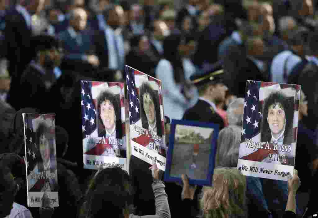 People hold up signs with the names and pictures of victims of the 9/11 terrorist attacks during a ceremony at ground zero in New York, Sept. 11, 2017. 