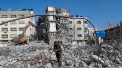 A backhoe removes parts of a building damaged by Israeli airstrikes last May, as a worker recycles metal from the rubble, in the central of al-Rimal neighborhood of Gaza City, Jan. 10, 2022.