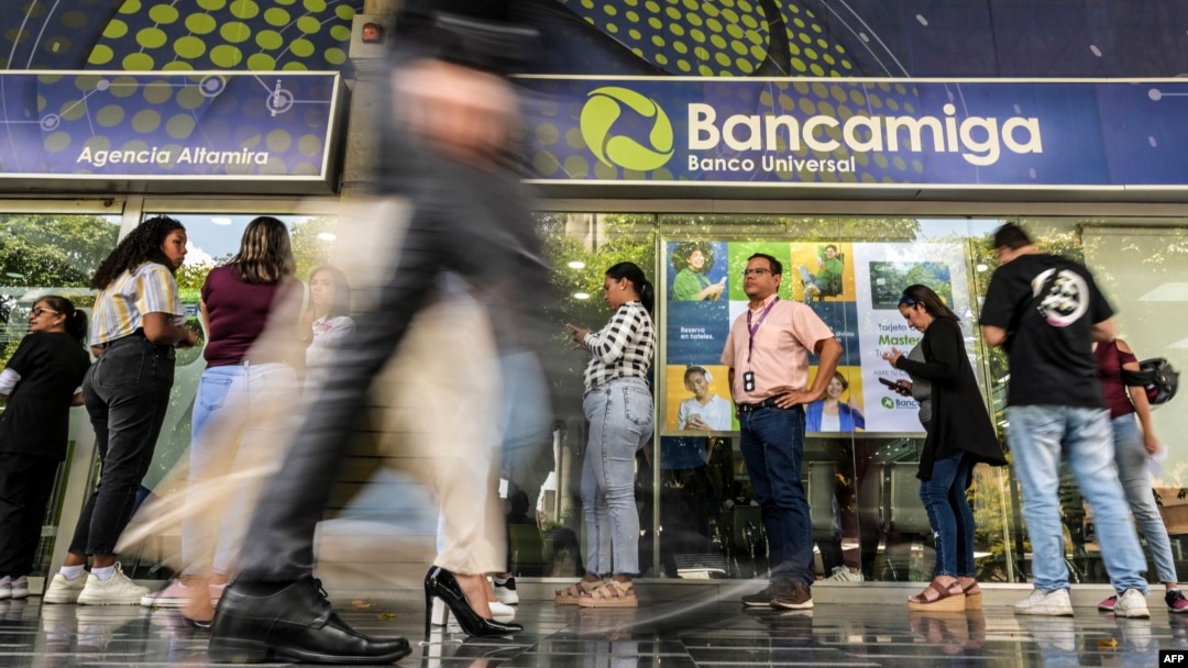 Un grupo de personas aguarda a las afueras de una sede del banco venezolano Bancamiga en Caracas, el 22 de abril de 2024. Tres de los socios accionistas de esa entidad financiera fueron detenidos por el gobierno por presunta corrupción.