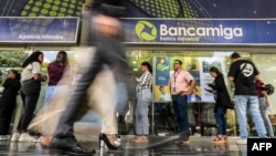Un grupo de personas aguarda a las afueras de una sede del banco venezolano Bancamiga en Caracas, el 22 de abril de 2024. Tres de los socios accionistas de esa entidad financiera fueron detenidos por el gobierno por presunta corrupción.