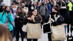 People carry shopping bags while others queue to enter a store on Oxford Street in London, Monday, April 12, 2021. 