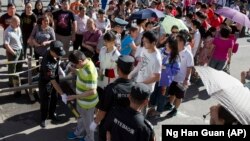 A security guard use a metal detector to check students arriving for the annual Gaokao or national college entrance exam held at a school in Beijing, Sunday, June 7, 2015. (AP Photo/Ng Han Guan)