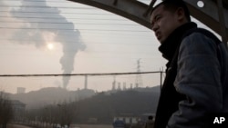 FILE - In this Dec. 30, 2016 photo, a man looks up near smoke spewing from a chimney near the Jiujiang steel and rolling mills in Qianan in northern China's Hebei province.