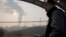 FILE - In this Dec. 30, 2016 photo, a man looks up near smoke spewing from a chimney near the Jiujiang steel and rolling mills in Qianan in northern China's Hebei province.