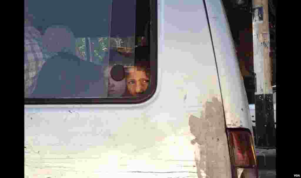 A child peers out of a micro bus window into traffic. (J. Weeks/VOA)