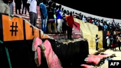 People stand before a collapsed wall at Demba Diop stadium, July 15, 2017, in Dakar after a soccer game between local teams Ouakam and Stade de Mbour. Eight people were killed during Senegal's football league final, in a stampede that broke out following clashes at the end of the match, the official APS news agency said. The wall collapse added many more to be injured. 