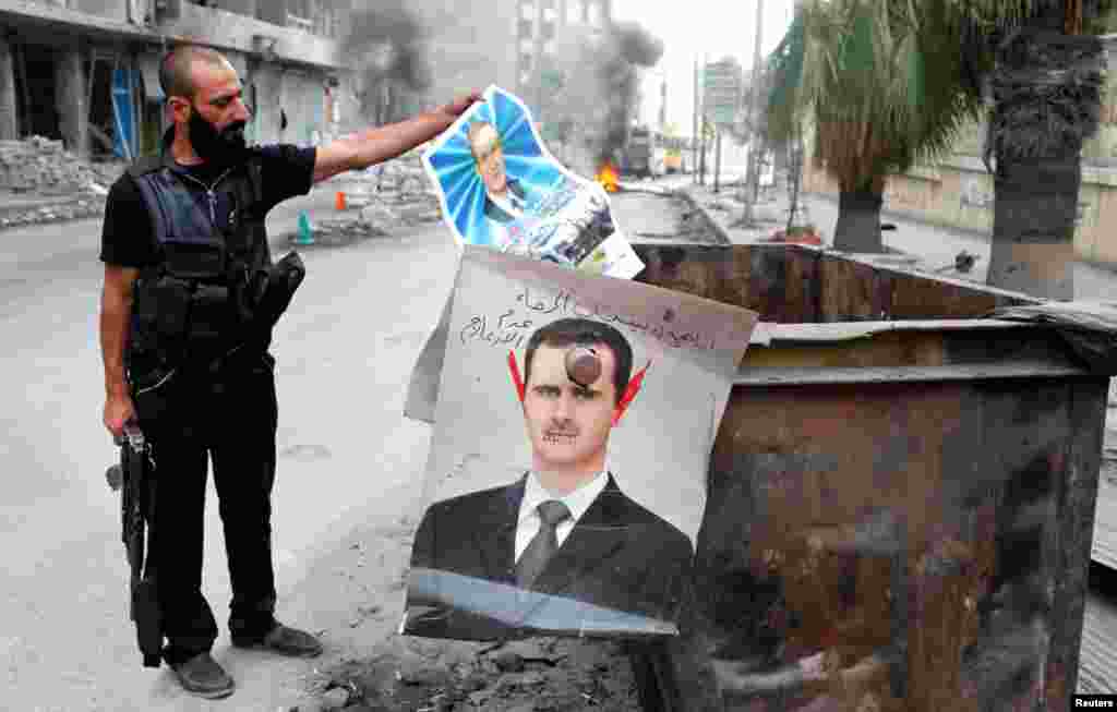 A member of the Free Syrian Army holds up a poster of Hafez al-Assad, the father of current President Bashar al-Assad whose defaced picture hangs on a garbage bin in Aleppo, October, 17, 2012.