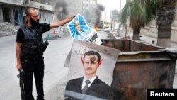 A member of the Free Syrian Army holds up a poster of Hafez al-Assad, the father of current President Bashar al-Assad whose defaced picture is seen hanging on a garbage bin near an area that they set fire to in the city of Aleppo, October, 17, 2012.