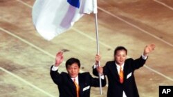 Foto sa a montre Pak Jung Chul (goch), antrenè ekip judo Kore di Nò a, ak Chung Eun-sun, jwè baskèt Kore di Sid, ki t ap pote ansanm drapo inite a nan Je Zolenpik Sydney a nan Ostrali, le 15 septanm 2000.