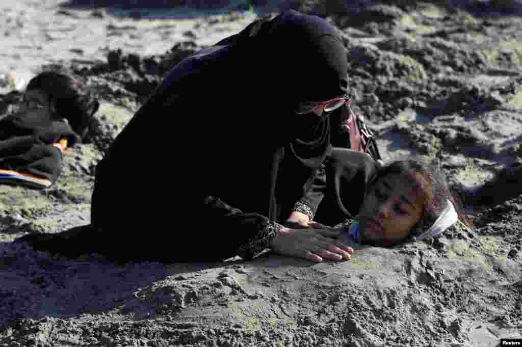 A woman comforts her daughter, buried up to her neck in sand during a solar eclipse, along Clifton beach in Karachi, Pakistan. Many Pakistanis believe that burying people with disabilities in sand during solar eclipse would bring healing to their bodies.