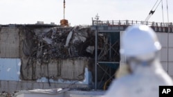 A member of the media tour group wearing a protective suit and a mask looks at the No. 3 reactor building at Tokyo Electric Power Co's (TEPCO) tsunami-crippled Fukushima Dai-ichi nuclear power plant in Okuma, Fukushima Prefecture, Japan, Feb. 10, 2016. A devastating earthquake and tsunami struck on March 11, 2011, and left nearly 19,000 people dead or missing, turned coastal communities into wasteland and triggered a nuclear crisis.