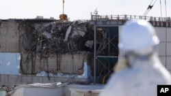 A member of the media tour group wearing a protective suit and a mask looks at the No. 3 reactor building at Tokyo Electric Power Co's (TEPCO) tsunami-crippled Fukushima Daiichi nuclear power plant in Okuma, Fukushima Prefecture, Japan, Feb. 10, 2016. 