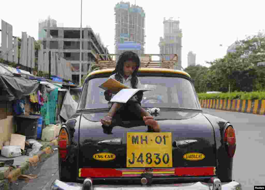 A girl studies while sitting on top of a taxi outside her shanty home at a roadside in Mumbai, India.